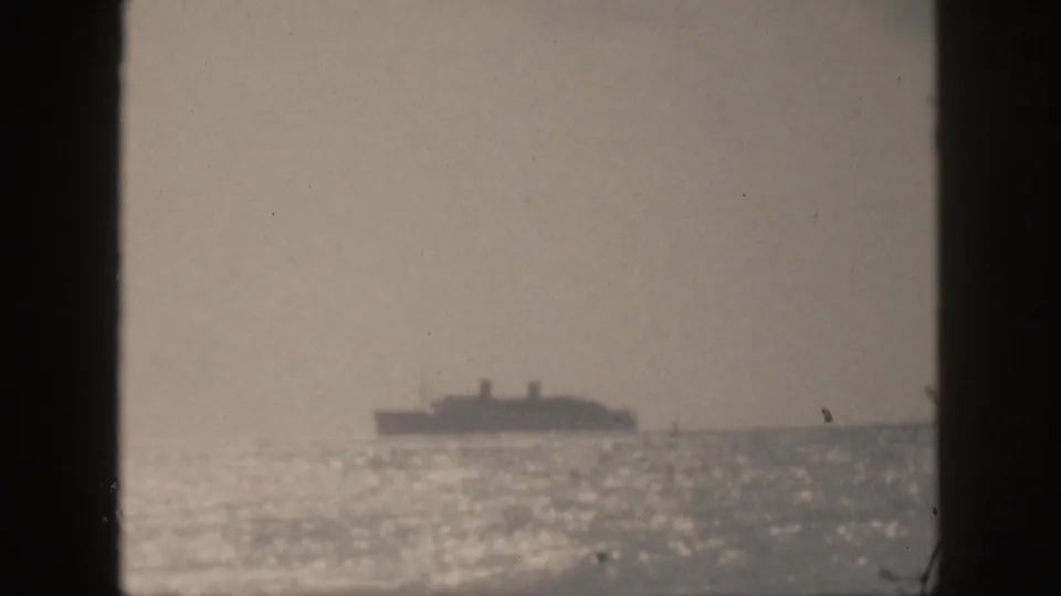 1959 Hawaii home-movie frame with a soft, distant ship silhouetted against haze above glittering ocean water.