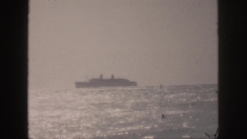 1959 Hawaii 8mm frame showing a far passenger ship on a bright, hazy ocean horizon, viewed through dark vertical framing.
