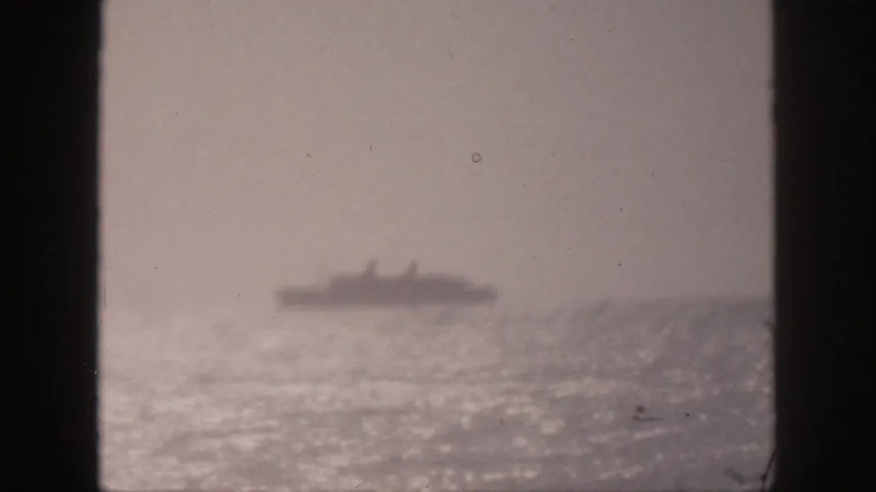 Soft 1959 Hawaii home-movie view of a distant ship across reflective ocean water, partially framed by dark vertical edges.
