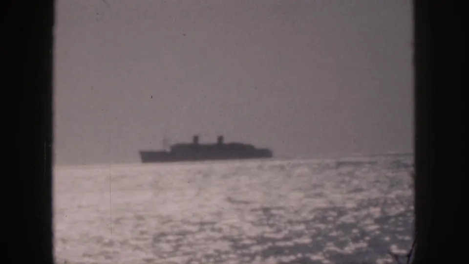 1959 Hawaii home-movie frame showing a distant ship silhouette over rippled ocean water, with haze and visible film grain.