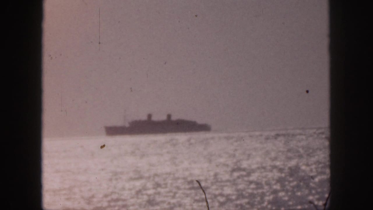 1959 Hawaii 8mm frame showing a distant ship at sea through vertical window framing, with glare on the water and a muted sky.