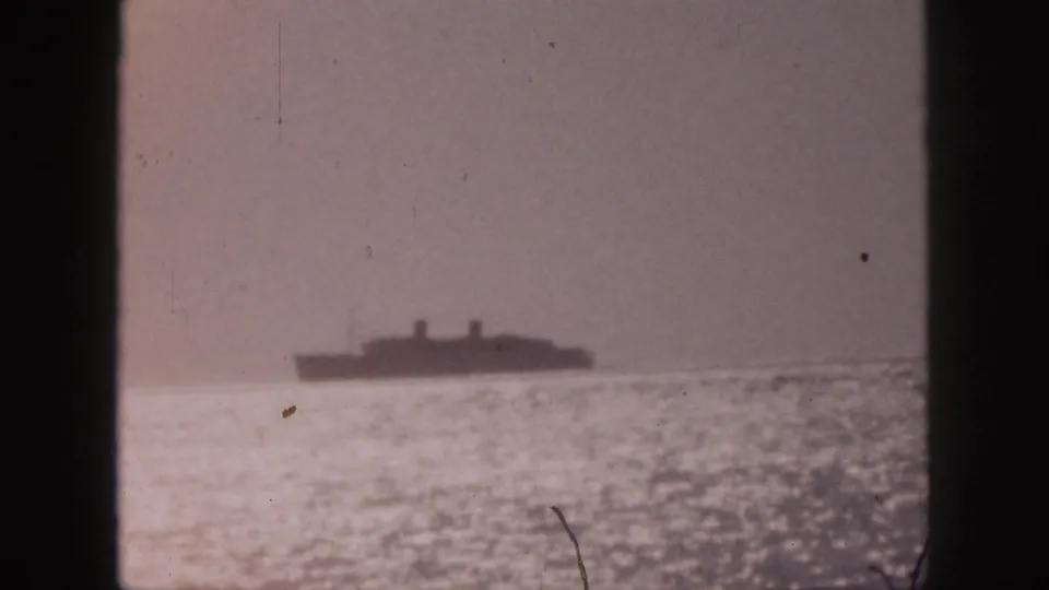 1959 Hawaii 8mm frame showing a distant ship at sea through vertical window framing, with glare on the water and a muted sky.