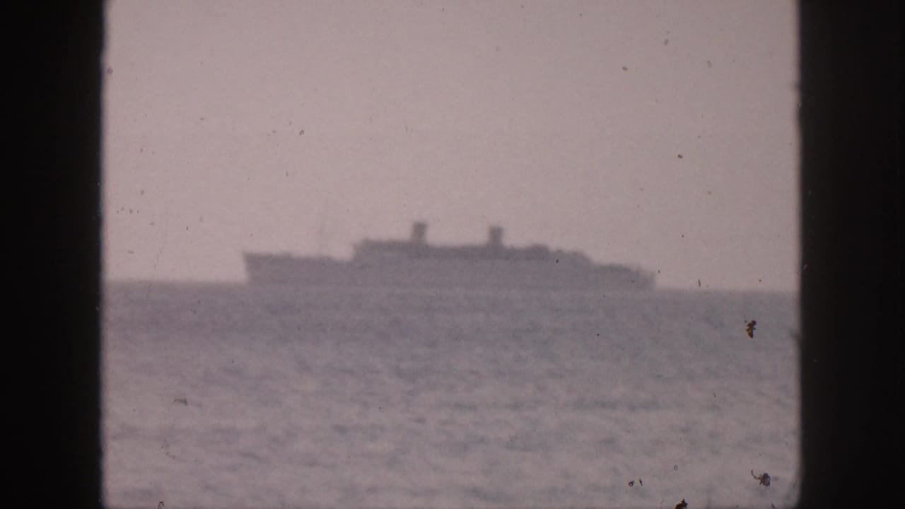 Large distant ship on open water, partially divided by a dark window frame.