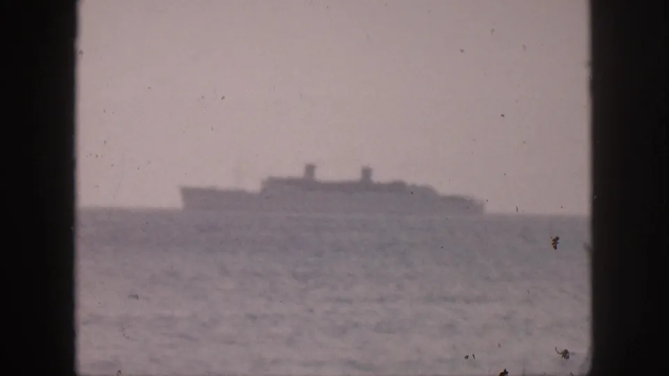 A large cruise ship or passenger vessel appears far offshore in a hazy 1959 Hawaii home-movie frame divided by window mullions.