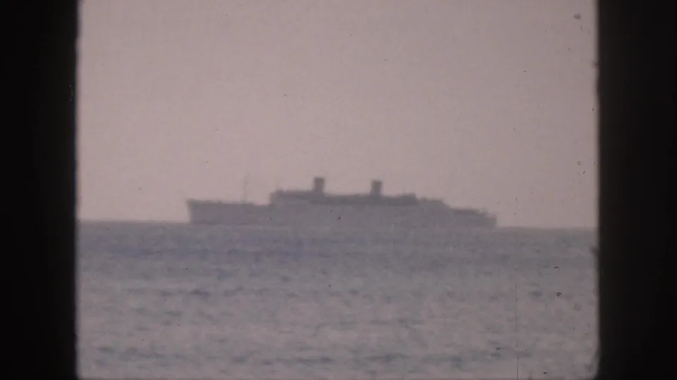 A hazy 1959 Hawaii 8mm frame shows a distant passenger ship at sea beyond dark window edges and a lightly rippled ocean.