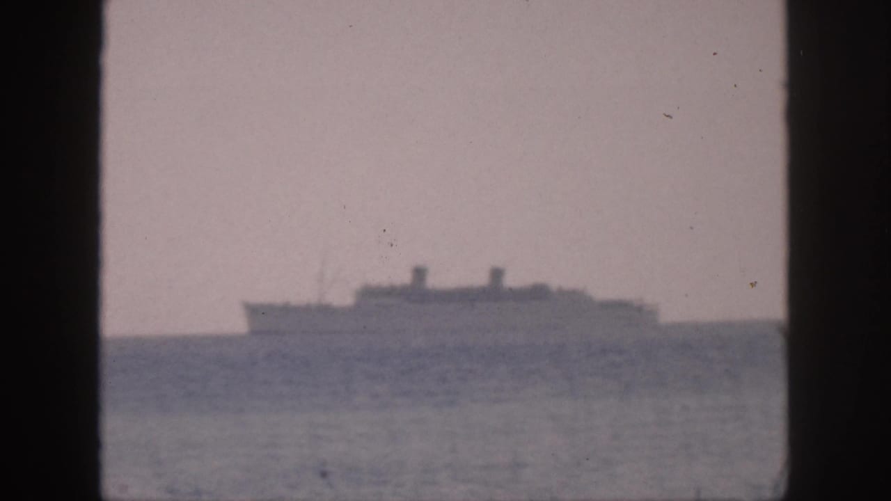 1959 Hawaii 8mm frame showing a distant passenger ship on a smooth ocean under a cloudy sky, viewed through dark borders.