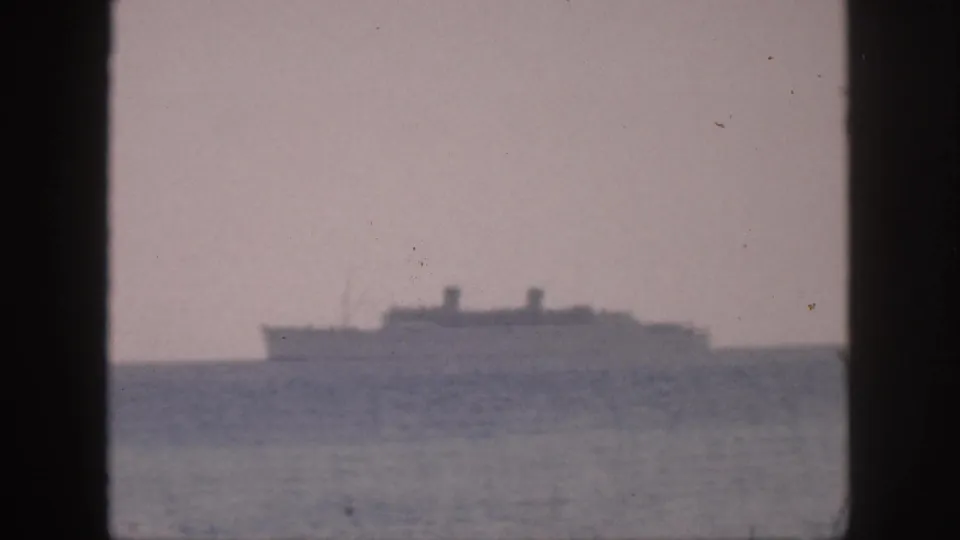 1959 Hawaii 8mm frame showing a distant passenger ship on a smooth ocean under a cloudy sky, viewed through dark borders.