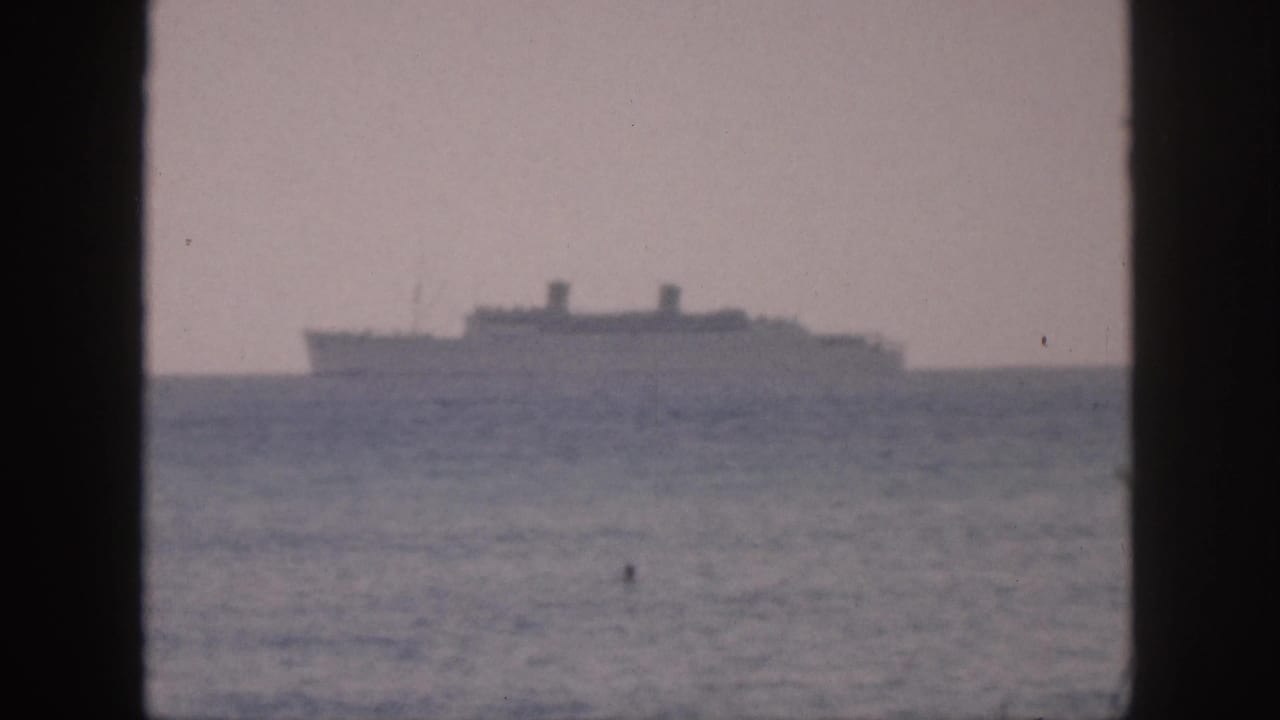 1959 Hawaii 8mm frame showing a distant ocean liner silhouette beyond hazy sea, viewed through dark vertical frame bars.