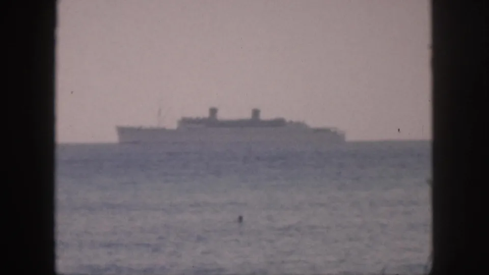 1959 Hawaii 8mm frame showing a distant ocean liner silhouette beyond hazy sea, viewed through dark vertical frame bars.