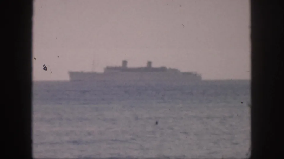 A faded 8mm view of a large ship sailing offshore in Hawaii, framed by dark vertical bars and a hazy sky.
