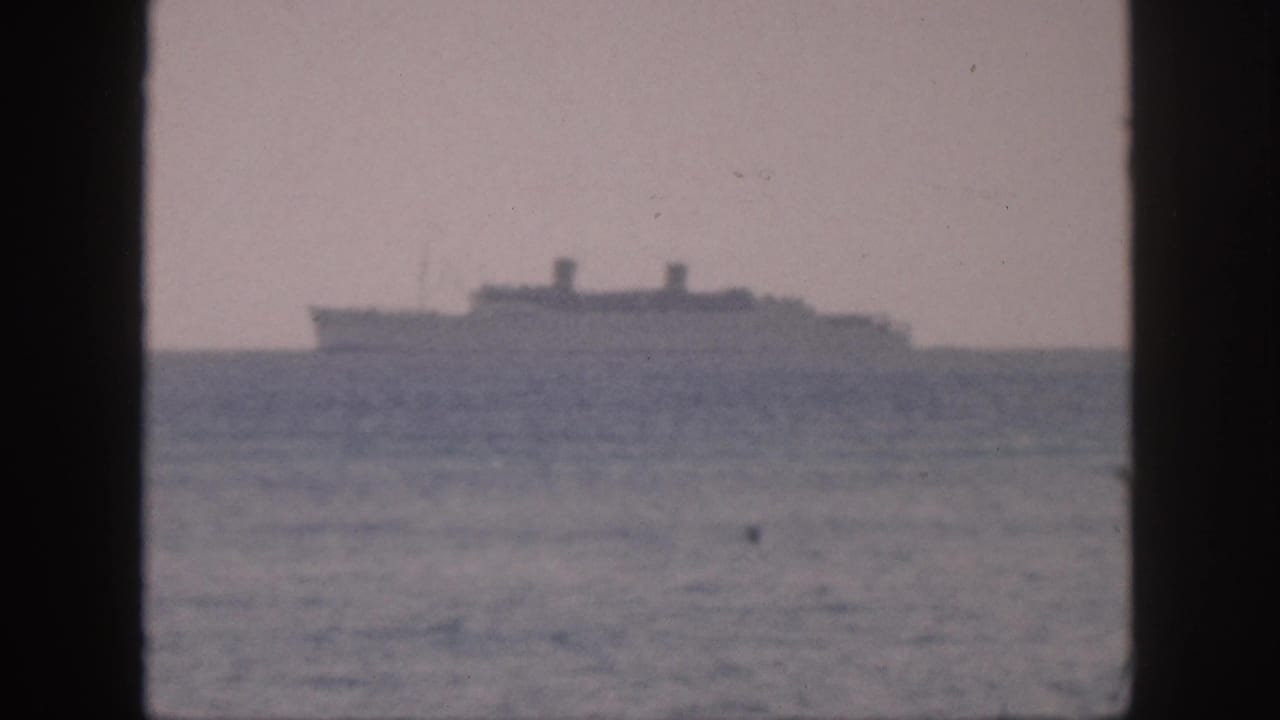 Soft-focus 1959 Hawaii home-movie frame with a distant ship above the ocean, seen through a dark window-like foreground frame.