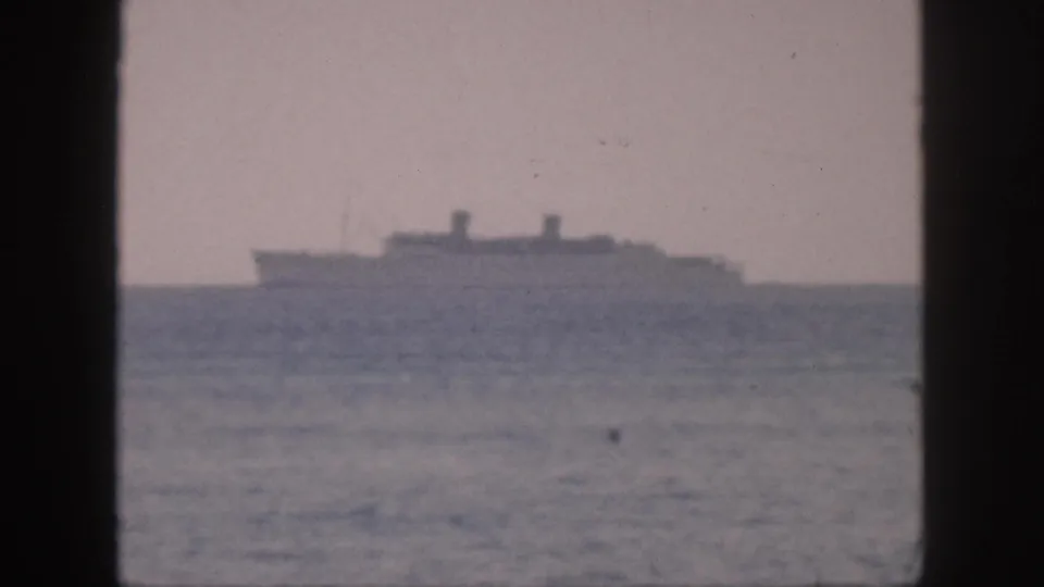 Soft-focus 1959 Hawaii home-movie frame with a distant ship above the ocean, seen through a dark window-like foreground frame.