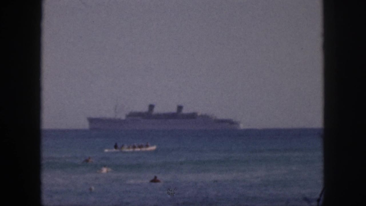 1959 Hawaii 8mm frame showing a small boat carrying people in the foreground with a larger ship farther out at sea.