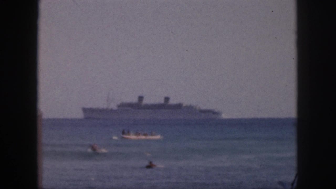 1959 Hawaii beach footage shows swimmers and a small motorboat in the foreground, with a large distant ship under a hazy sky.