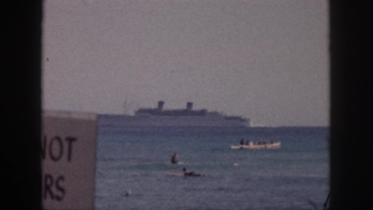 A large distant ship remains near the horizon as swimmers and a small boat move across the water, with partial sign lettering at left.