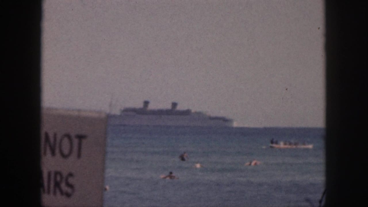 1959 Hawaii beach view with swimmers in the water, a distant passenger ship, a small boat, and a partly readable sign near the center-left.