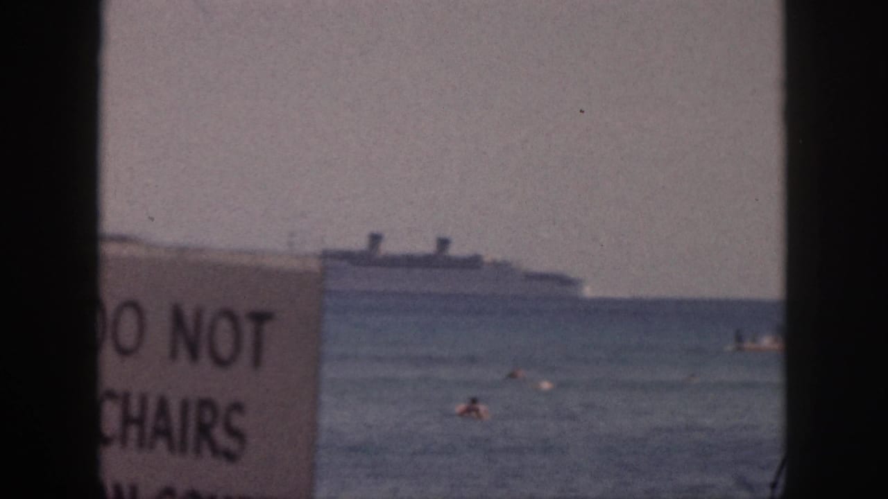 1959 Hawaii 8mm frame with a cropped sign reading parts of 'DO NOT' and 'CHAIRS,' swimmers in the water, and an ocean liner offshore.