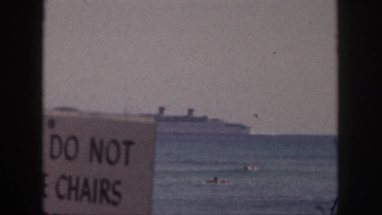 1959 Hawaii beach frame showing a cropped 'DO NOT' and 'CHAIRS' sign in front of swimmers and a distant passenger ship.