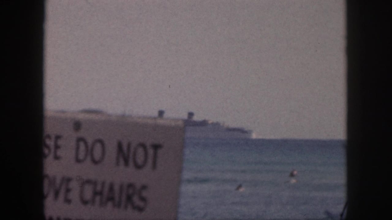 A 1959 Hawaii shoreline angle shows swimmers below a distant liner, partly obscured by a DO NOT MOVE CHAIRS sign.
