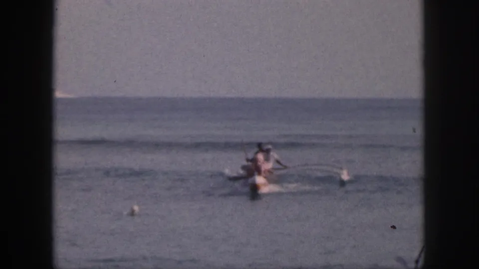The canoe continues across open Hawaii water, with paddlers, small buoys, and a flat horizon visible in the 8mm frame.