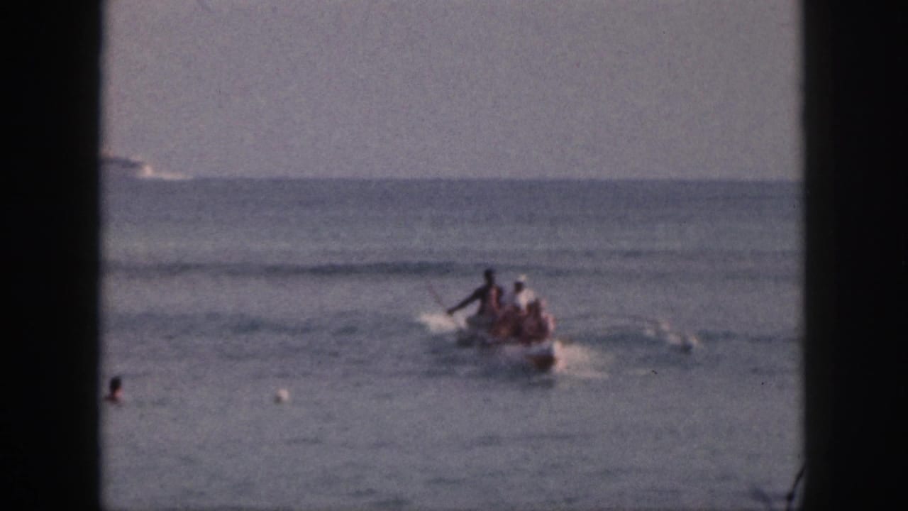 1959 Hawaii home-movie frame showing a small motorboat with passengers crossing calm water while swimmers and buoys appear nearby.