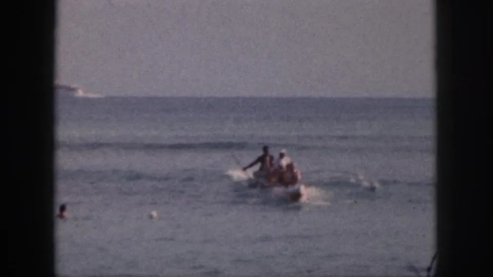 1959 Hawaii home-movie frame showing a small motorboat with passengers crossing calm water while swimmers and buoys appear nearby.
