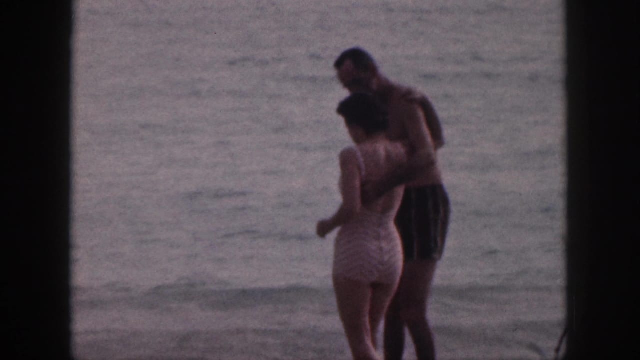 The couple stands facing each other in shallow water near the shoreline.