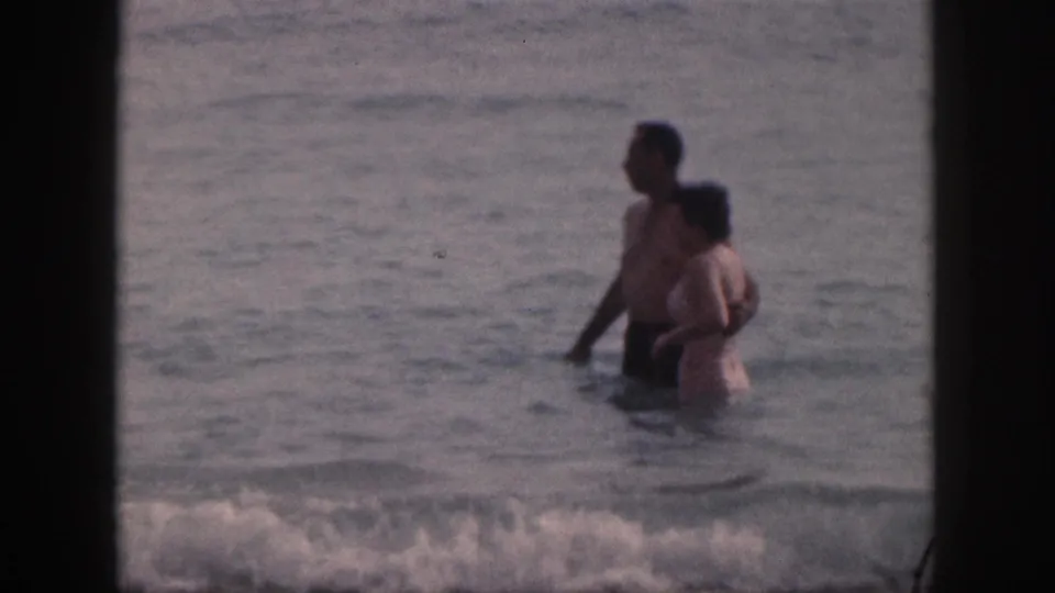 In the final frame, the couple stands close in the Hawaii surf as foamy water crosses the lower edge of the 8mm frame.
