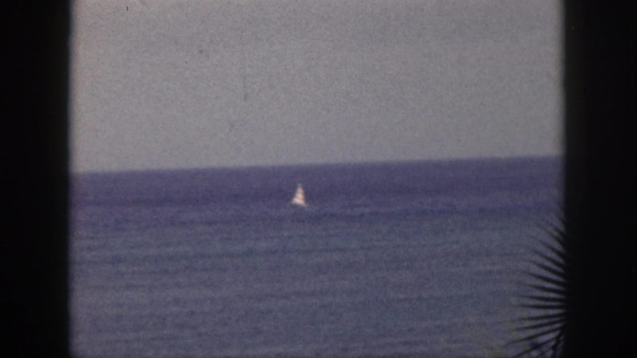 1959 Hawaii 8mm frame showing a small white sailboat far out on the ocean, seen through dark foreground edges under a gray sky.