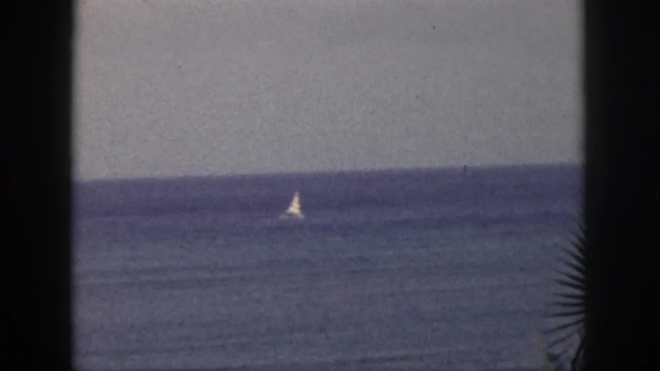 1959 Hawaii 8mm view of a distant sailboat on the ocean, with dark frame edges and a muted, grainy color palette.