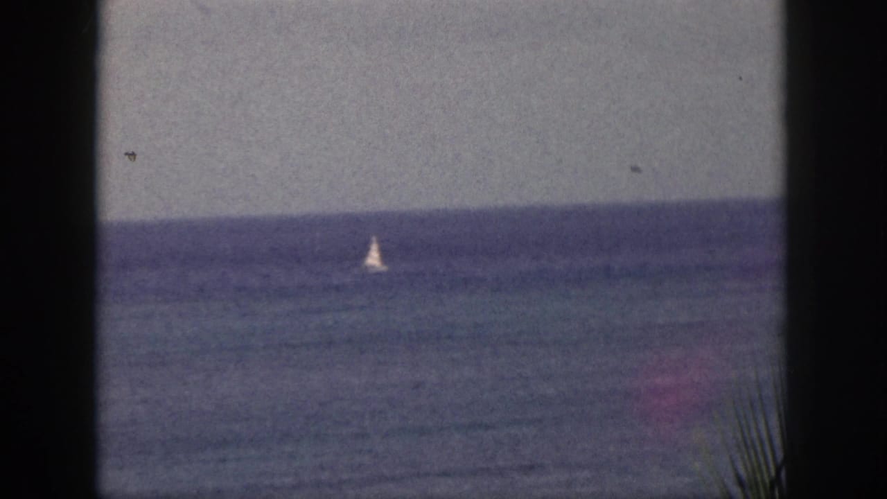 Distant sailboat on a blue ocean seen through dark vertical frame edges.