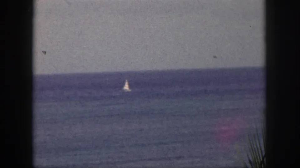 1959 Hawaii 8mm view of a small sailboat on the ocean, framed by dark foreground edges and a level horizon.