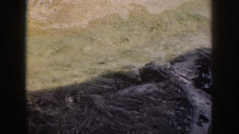 1959 Hawaii 8mm frame looking across dark wet rocks and shallow water within the seal enclosure.