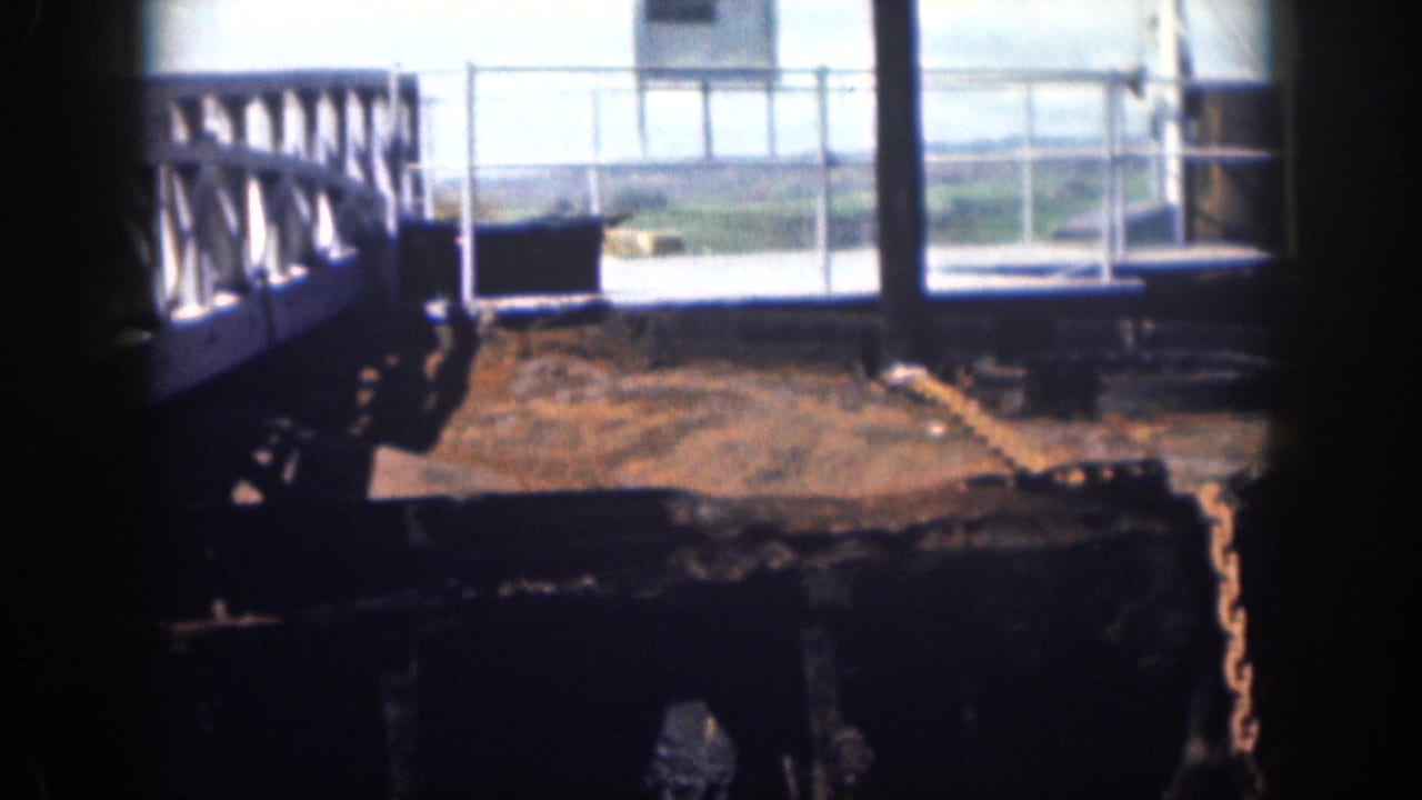 Corroded dock platform with railings, posts, and a hanging chain near water.