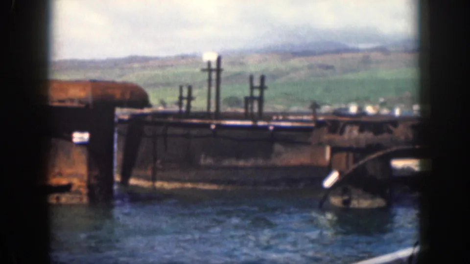 1959 Hawaii home-movie frame showing cylindrical concrete forms, a pier edge, choppy water, and green hills from a boat viewpoint.