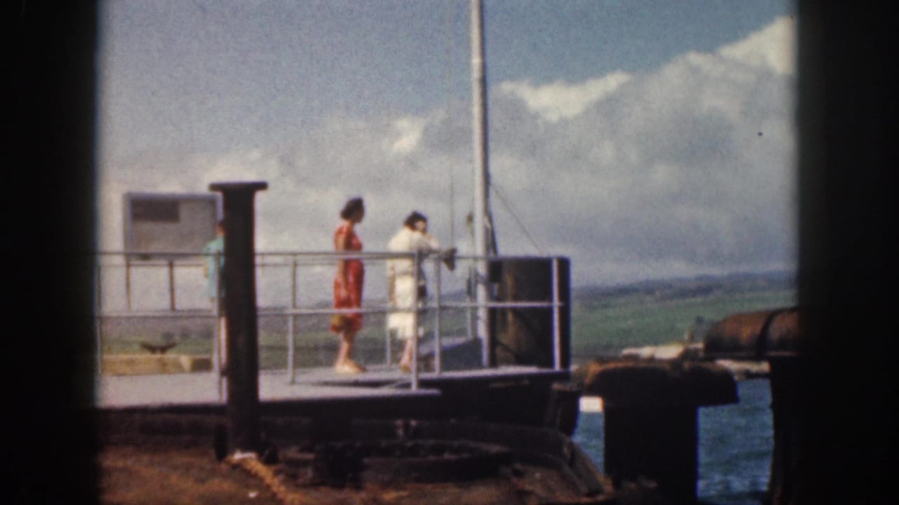 1959 Hawaii home-movie frame showing people at a naval station dock railing, including a woman in red and a person in white, looking over the water.