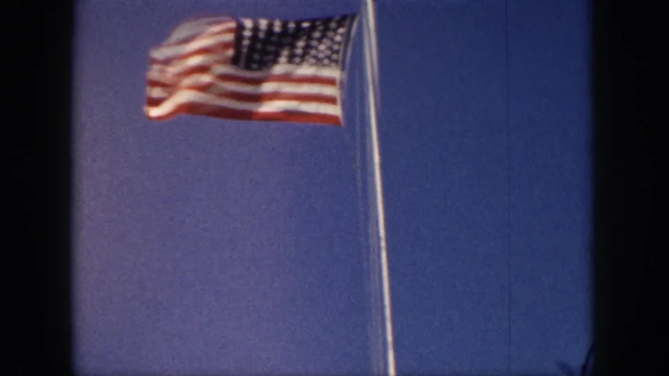 Close view from 1959 Hawaii footage of a U.S. flag moving in the wind on a tall pole, framed against open blue sky.