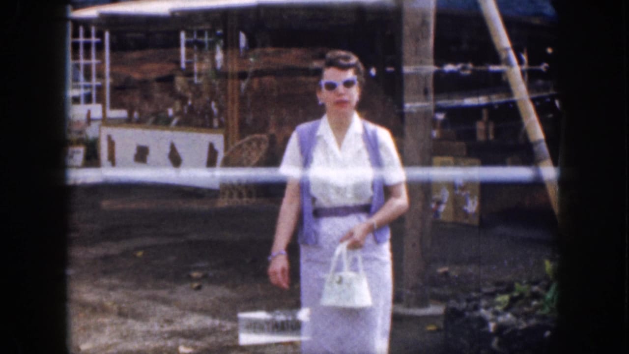 Woman in sunglasses approaches the camera while carrying a white handbag.