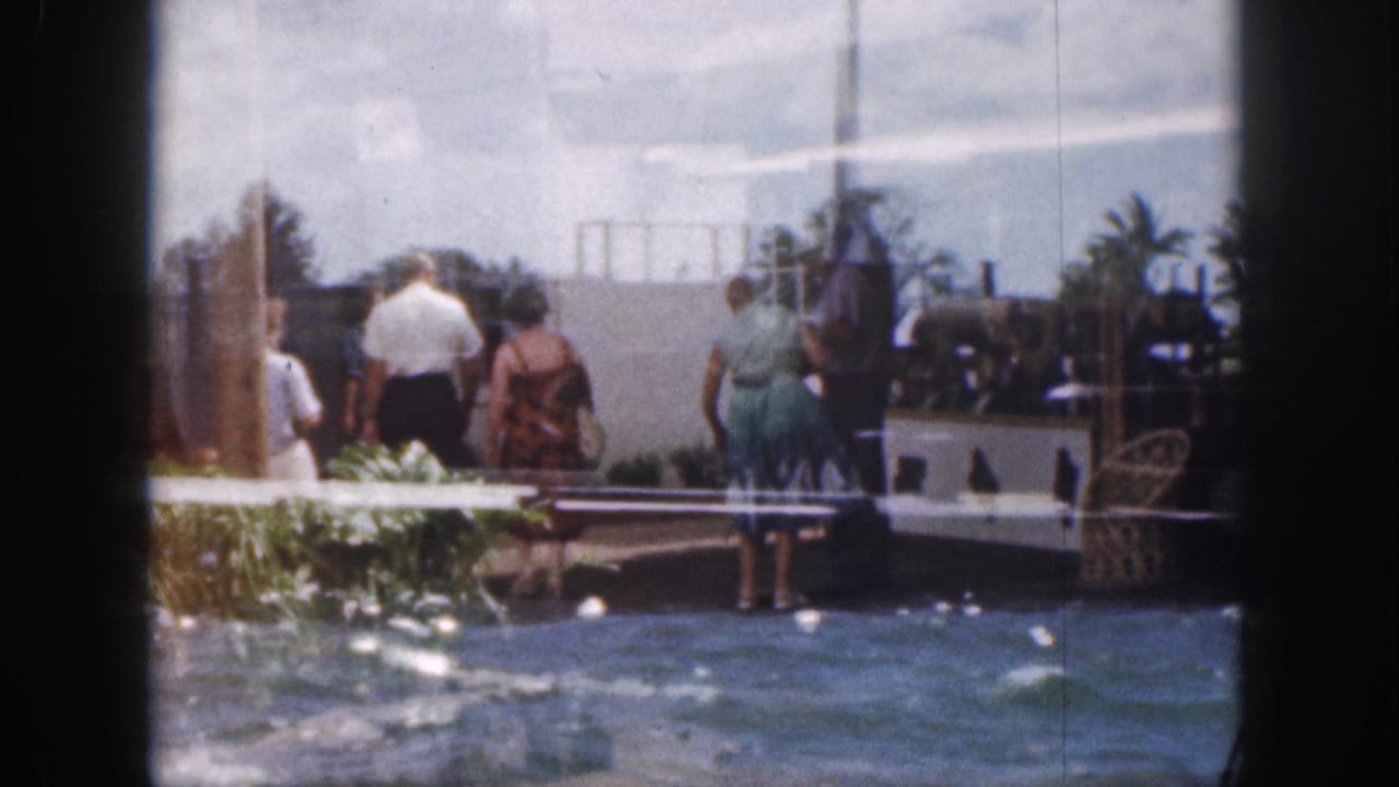 Adults continue along the pier near water, plants, railings, and shaded resort features.