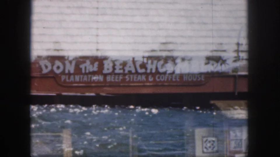 1959 Hawaii home-movie frame holding on the Don the Beachcomber waterfront sign, water, railings, and resort building facade.
