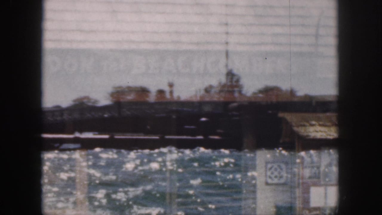 1959 Hawaii frame showing bright water and low pier structures with faint double-exposed signage across the upper area.