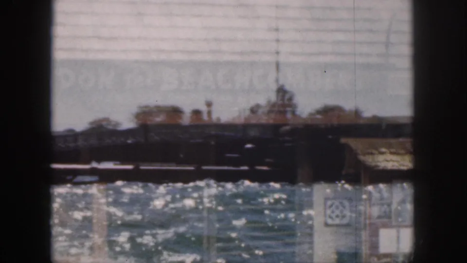1959 Hawaii frame showing bright water and low pier structures with faint double-exposed signage across the upper area.