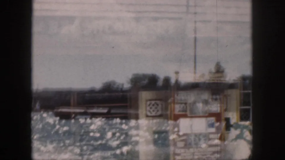 1959 Hawaii 8mm frame with a small waterfront building, sparkling water, and ghosted commercial lettering from the overlapping exposure.