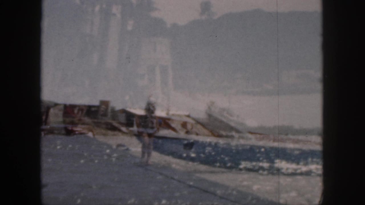 Man continues along the waterfront with small boats and water in the background.