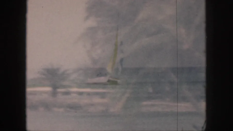 A distant surfer stands on a board in gentle Hawaii surf, with visible 8mm grain and faded color.