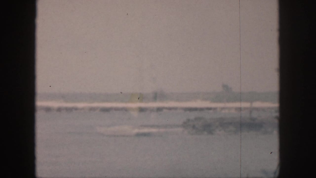 1959 Hawaii 8mm view of a quiet waterfront, with a low distant shore and faint palm shapes under a pale sky.