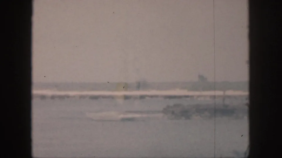 1959 Hawaii 8mm view of a quiet waterfront, with a low distant shore and faint palm shapes under a pale sky.