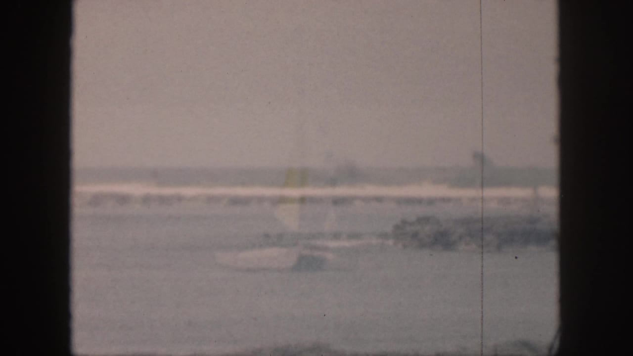 Distant ocean surf seen through dark vertical window frames on faded 8mm film.