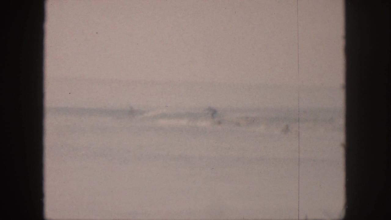 Hazy ocean surface with faint distant surfers and dark film-frame edges.