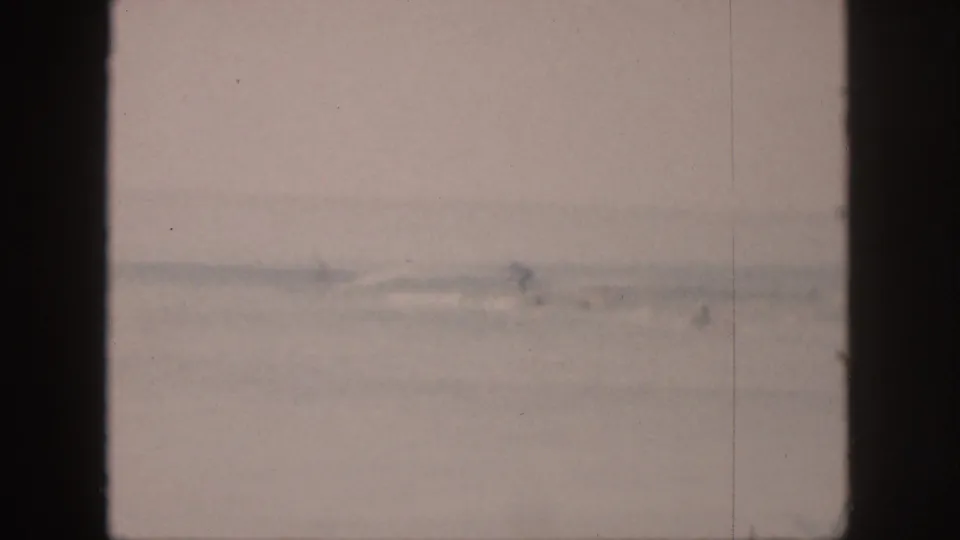 1959 Hawaii 8mm frame showing hazy shallow surf with tiny distant surfer silhouettes near shore.